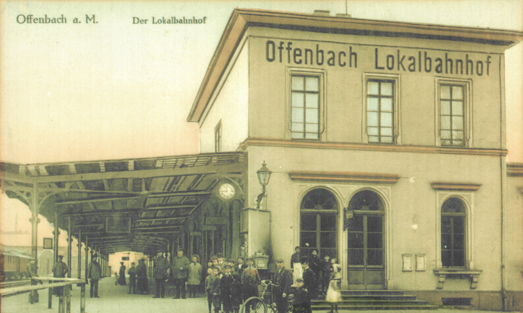 Das historische Bahnhofsgebäude mit wartenden Fahrgästen.